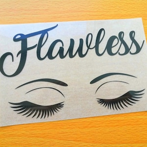 Puede incluir: Una calcomanía de vinilo negro con la palabra "Flawless" en escritura cursiva sobre un par de ojos cerrados con largas pestañas. La calcomanía está sobre un respaldo transparente, sobre una superficie amarillo-naranja.