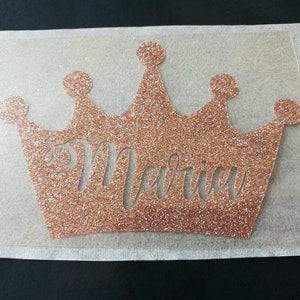 Puede incluir: Una corona de hierro con purpurina dorada rosa con el nombre "Marissa" recortado en el centro.