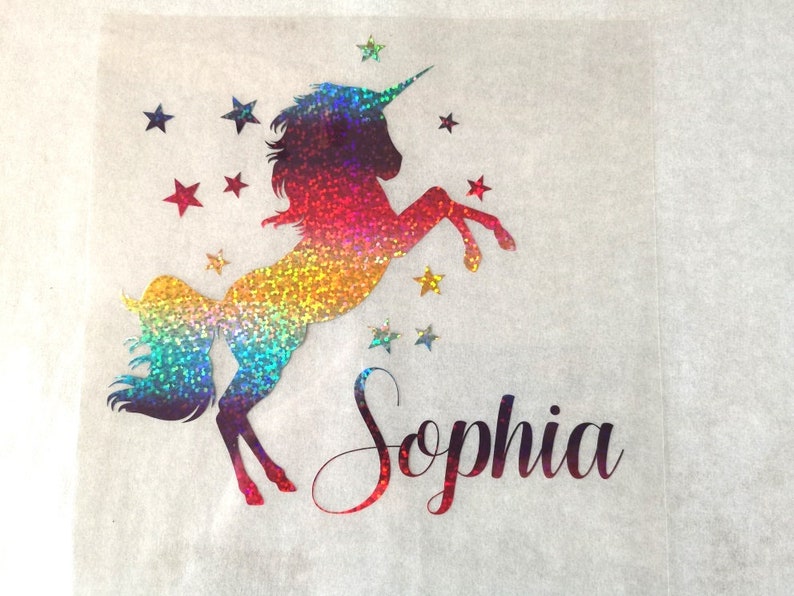May include: A rainbow glitter unicorn with a horn and a star design. The unicorn is standing on its hind legs with its front legs raised. The name "Sophia" is written below the unicorn.