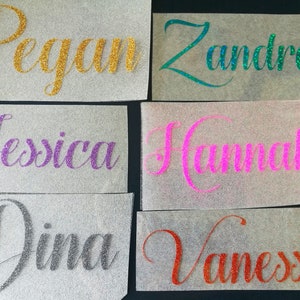 Pode incluir: Seis nomes, incluindo "Pegan", "Zandra", "Jessica", "Hannah", "Dina" e "Vanessa", são escritos em letras brilhantes de glitter em papel branco.