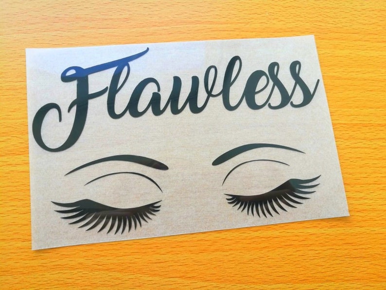 May include: A black vinyl decal featuring the word "Flawless" in elegant script above a pair of closed eyes with long eyelashes. The decal is on a transparent backing, set against a yellow-orange surface.