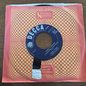 May include: A vintage 45 RPM vinyl record by Tommy Steele titled What A Mouth, featuring a dark blue center label with white text. The record is housed in a square paper sleeve with a red and yellow checkered pattern and United Artists Records logo.