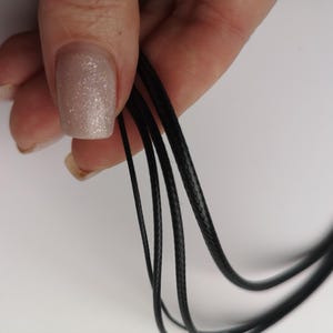 May include: Close-up of black waxed cord, showing the texture of the cord. The cord is held in a hand.