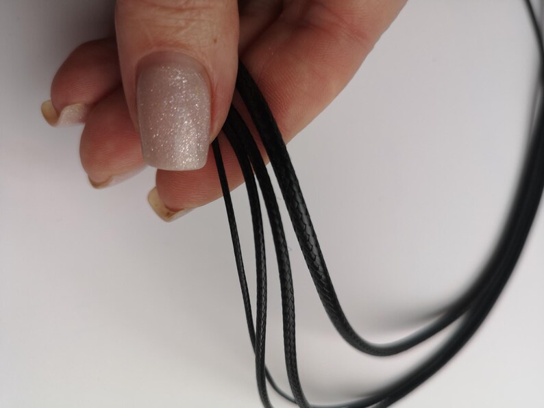 May include: Close-up of black waxed cord, showing the texture of the cord. The cord is held in a hand.