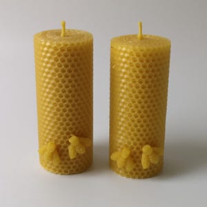 May include: Two yellow beeswax candles with a honeycomb pattern and three small bee decorations at the bottom of each candle.