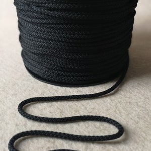 May include: A spool of black cord, with a length of the cord laid out on a light beige surface.