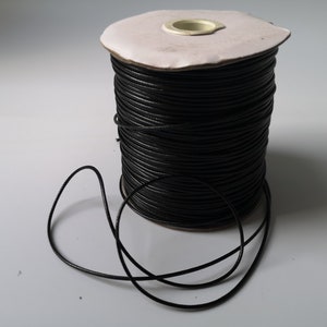 May include: A spool of black waxed cord, with a length of cord unwound and lying on a white surface.