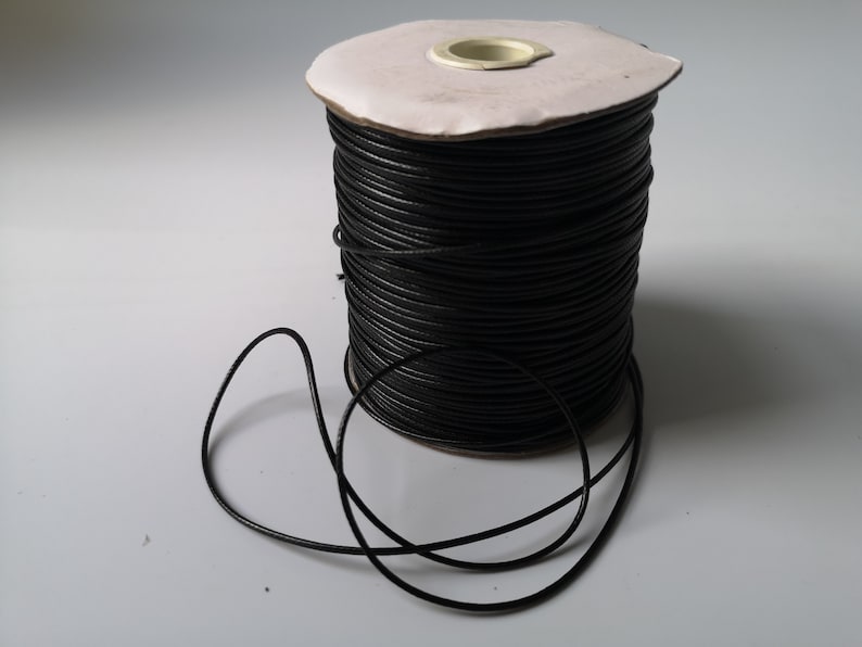 May include: A spool of black waxed cord, with a length of cord unwound and lying on a white surface.