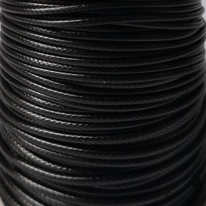 May include: Close-up of a spool of black waxed cotton cord. The cord is tightly wound and has a smooth, polished finish.