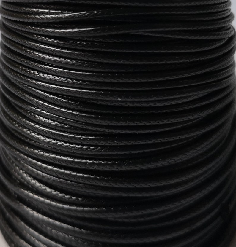 May include: Close-up of a spool of black waxed cotton cord. The cord is tightly wound and has a smooth, polished finish.