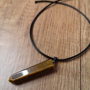 May include: A brown and gold tiger's eye crystal pendant on a black cord necklace.