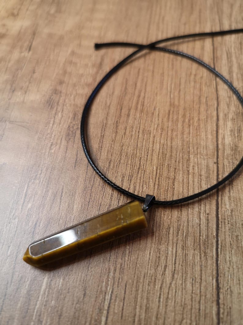 May include: A brown and gold tiger's eye crystal pendant on a black cord necklace.