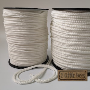 May include: Two spools of white cotton cord, each wound around a black plastic spool. The cord is approximately 3mm thick. A small brown tag with the text "2 little bees" is in the foreground.