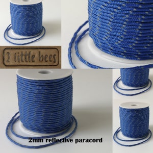 May include: A spool of 2mm reflective paracord in blue with a white reflective thread. The paracord is wound around a white spool and is labeled "2 little bees".