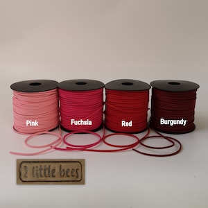 May include: Four spools of suede cord in pink, fuchsia, red, and burgundy. The spools are labelled with the colour names. The text "2 little bees" is printed on a brown label.