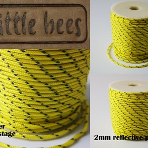 May include: A spool of 2mm yellow reflective paracord with black diamond-shaped stripes. The paracord is wound around a white cardboard core. The text "2mm reflective paracord" is printed below the spool.