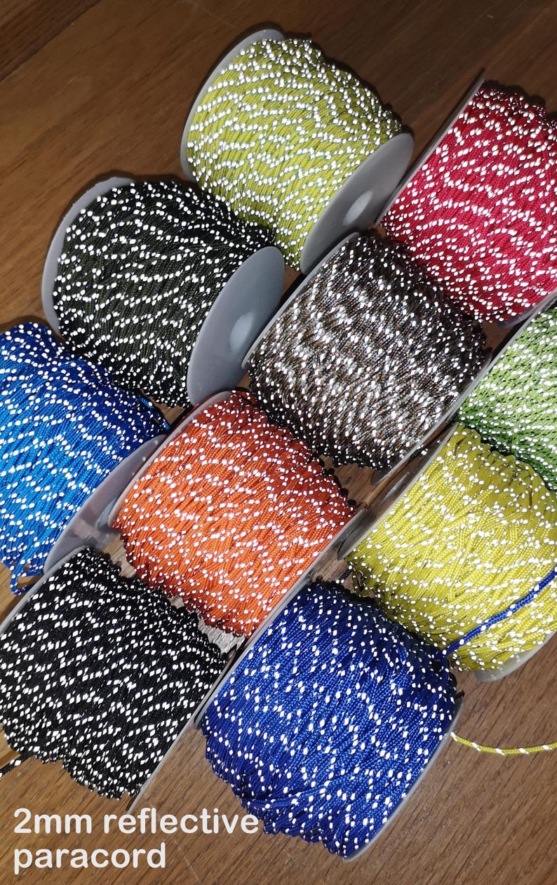May include: Assortment of 2mm reflective paracord spools in various colors, including black, blue, green, orange, red, and yellow. Each spool has white reflective threads woven into the paracord.