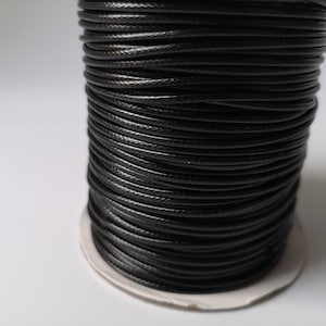 May include: A spool of black waxed cotton cord. The cord is wound tightly around the spool, creating a smooth, even surface.
