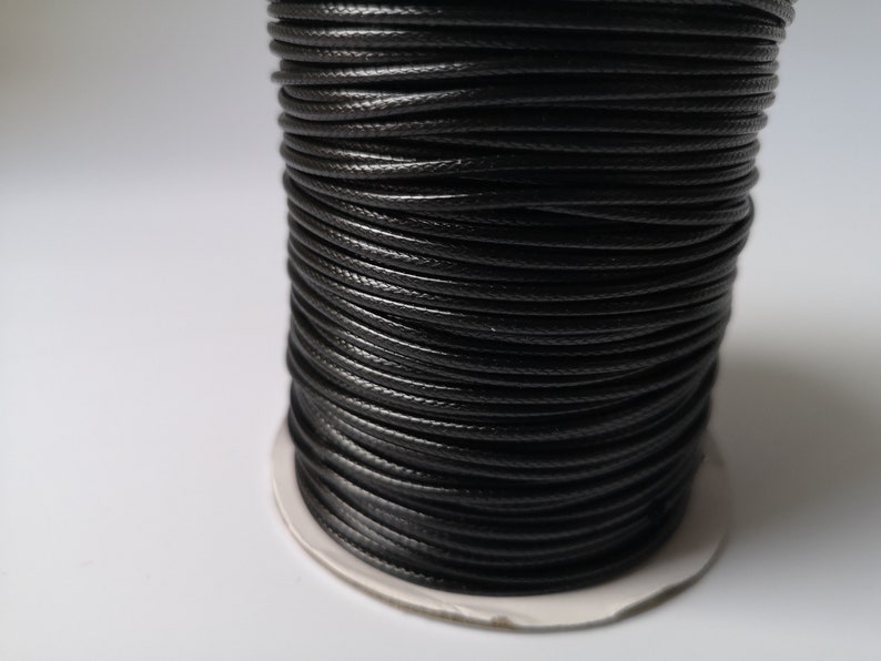 May include: A spool of black waxed cotton cord. The cord is wound tightly around the spool, creating a smooth, even surface.