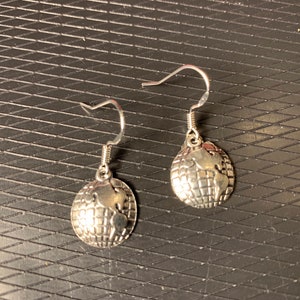 May include: A pair of silver-toned dangle earrings. Each earring features a small globe charm with detailed continents. The earrings have a simple hook design for easy wear. The globe charms are approximately 0.5 inches in diameter.