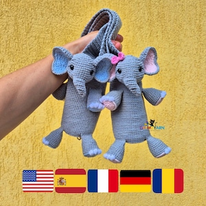 May include: Two grey crocheted elephant toys attached to a long grey crocheted strap. The left elephant has blue inner ears, while the right elephant features pink inner ears and a small pink bow. Both have black eyes and light blue foot pads.