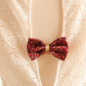 May include: A white lace dress with a low back and a red and gold bow tie accent.