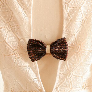 May include: White lace top with a low back and a black and gold bow tie accent.