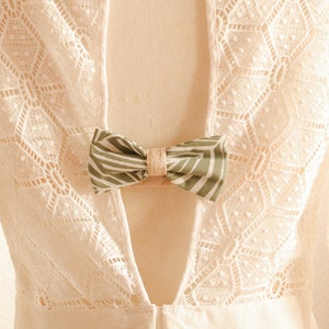 May include: White lace dress with a low back and a green and white bow tied at the back.