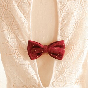 May include: White lace dress with a low back and a burgundy bow tie detail.