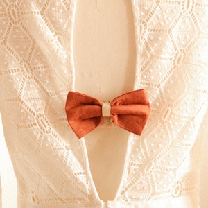 May include: White lace dress with a low back and a rust-colored bow tied at the back.