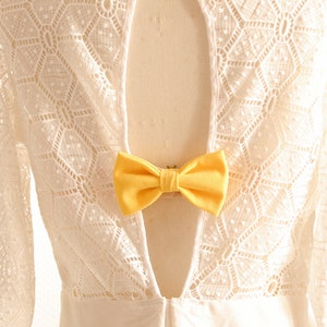 May include: White lace dress with a keyhole back and a yellow bow tie detail.