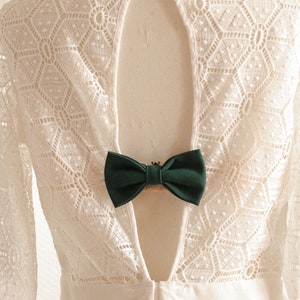May include: White lace dress with a deep V-back and a green bow accent.