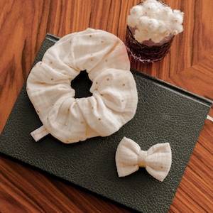 May include: A black notebook with a white fabric scrunchie and a white fabric bow with gold accents on top. The notebook is on a wooden surface.