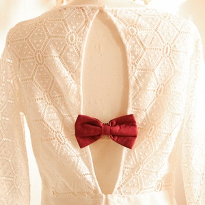 May include: White lace dress with a keyhole back and a burgundy bow tie detail.