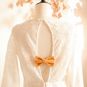 May include: White lace dress with a low back and a mustard yellow bow tie detail.