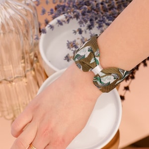 May include: A green and white patterned fabric hair tie tied in a bow on a person's wrist.