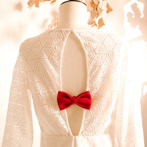 May include: White lace dress with a low back and a red bow tie detail.