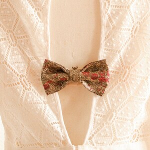 May include: White lace dress with a low back and a gold and red bow tied at the back.