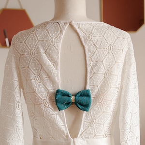 May include: White lace dress with a low back and a teal bow tie accent.
