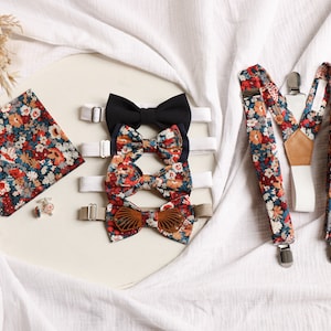 Può includere: Un set di papillon e bretelle con motivo floreale. I papillon sono di tre colori diversi: nero, rosso e marrone. Le bretelle sono bianche con motivo floreale. Il set include anche un fazzoletto da taschino con motivo floreale.