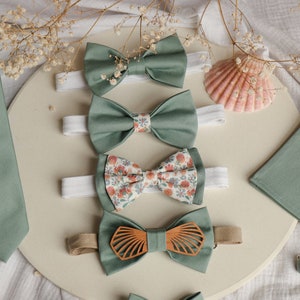 Puede incluir: Un conjunto de pajaritas de color verde salvia y una corbata, pañuelo de bolsillo y gemelos a juego. Las pajaritas presentan diferentes patrones, incluyendo un estampado floral y un diseño de concha de madera.