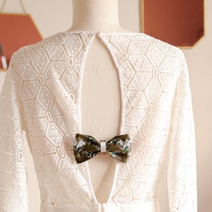 May include: White lace dress with a low back and a green and white bow tie accent.