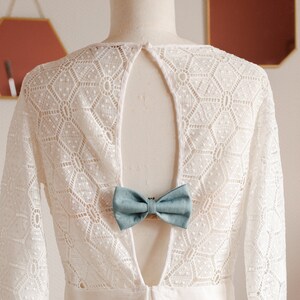 May include: White lace dress with a low back and a light blue bow tie accent.