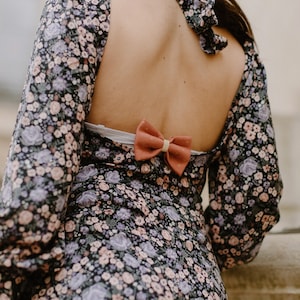 May include: A black floral dress with a low back and a coral bow tied at the back.