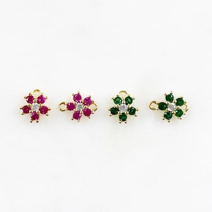 May include: Three gold flower-shaped charms with a loop for attaching to jewelry. The charms are decorated with small red, green, and clear gemstones.