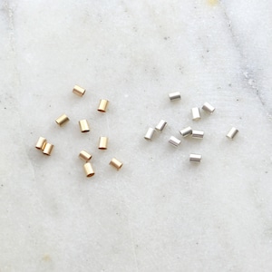 May include: A collection of gold and silver metal crimp beads. The beads are small and cylindrical in shape.