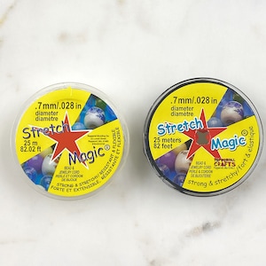 Puede incluir: Dos carretes de cordón elástico transparente para cuentas Stretch Magic. Los carretes son amarillos y negros con logotipos de estrellas rojas. El texto en los carretes dice "Stretch Magic" y "7 mm/0,028 pulgadas de diámetro". Los carretes tienen 25 metros o 82 pies de largo.