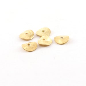 May include: Five gold-colored metal beads with a textured surface and a small hole in the center. The beads are shaped like a half-circle.