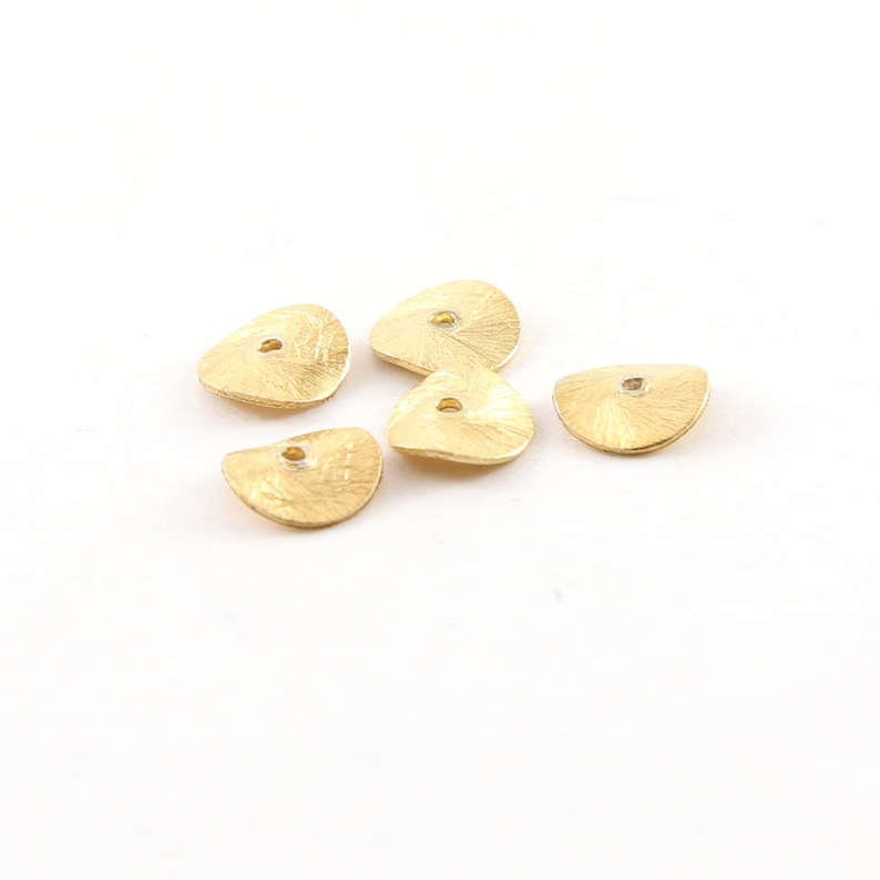 May include: Five gold-colored metal beads with a textured surface and a small hole in the center. The beads are shaped like a half-circle.