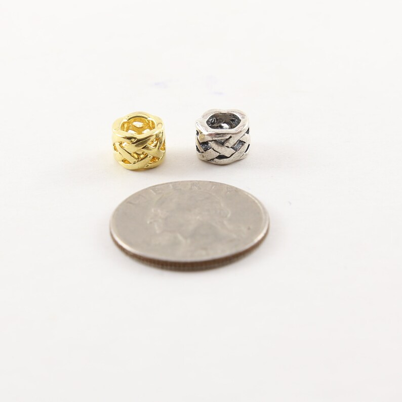 May include: Two small, decorative metal beads, one gold and one silver, with a woven design. The beads are about the size of a US quarter.